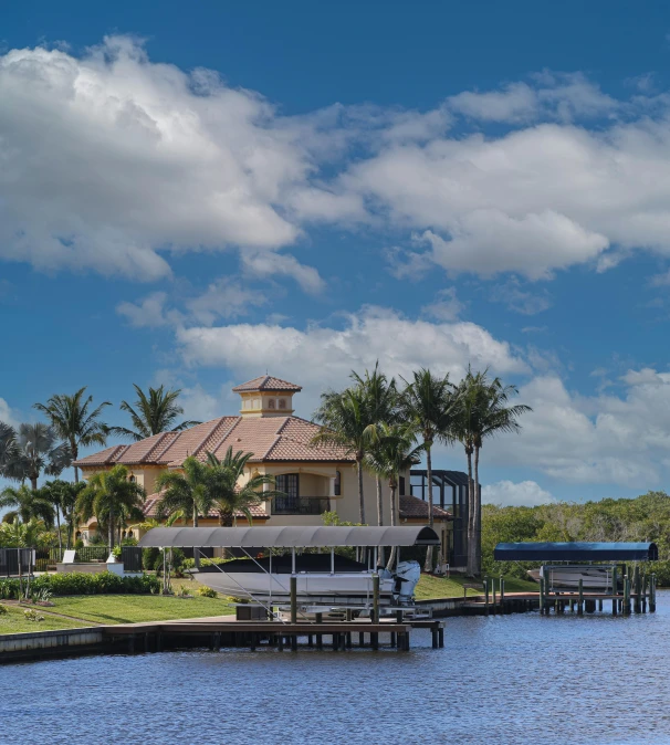 a house sitting on top of a lush green field next to a body of water, by Nicholas Marsicano, boat dock, kicking a florida mansion, today\'s featured photograph 4k, blue sky