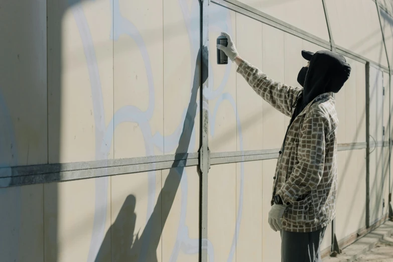 a man painting graffiti on the side of a building, an airbrush painting, by karlkka, unsplash, wide film still, metal cladding wall, profile image, cardboard