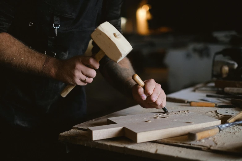 a man with a hammer working on a piece of wood, trending on pexels, arts and crafts movement, dwell, carved, schools, set on night