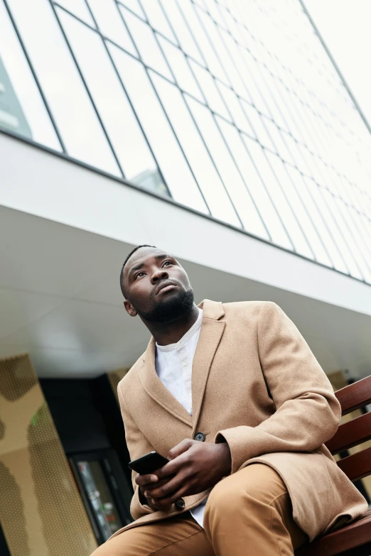 a man sitting on a bench holding a cell phone, light brown coat, mkbhd, human staring blankly ahead, instagram post