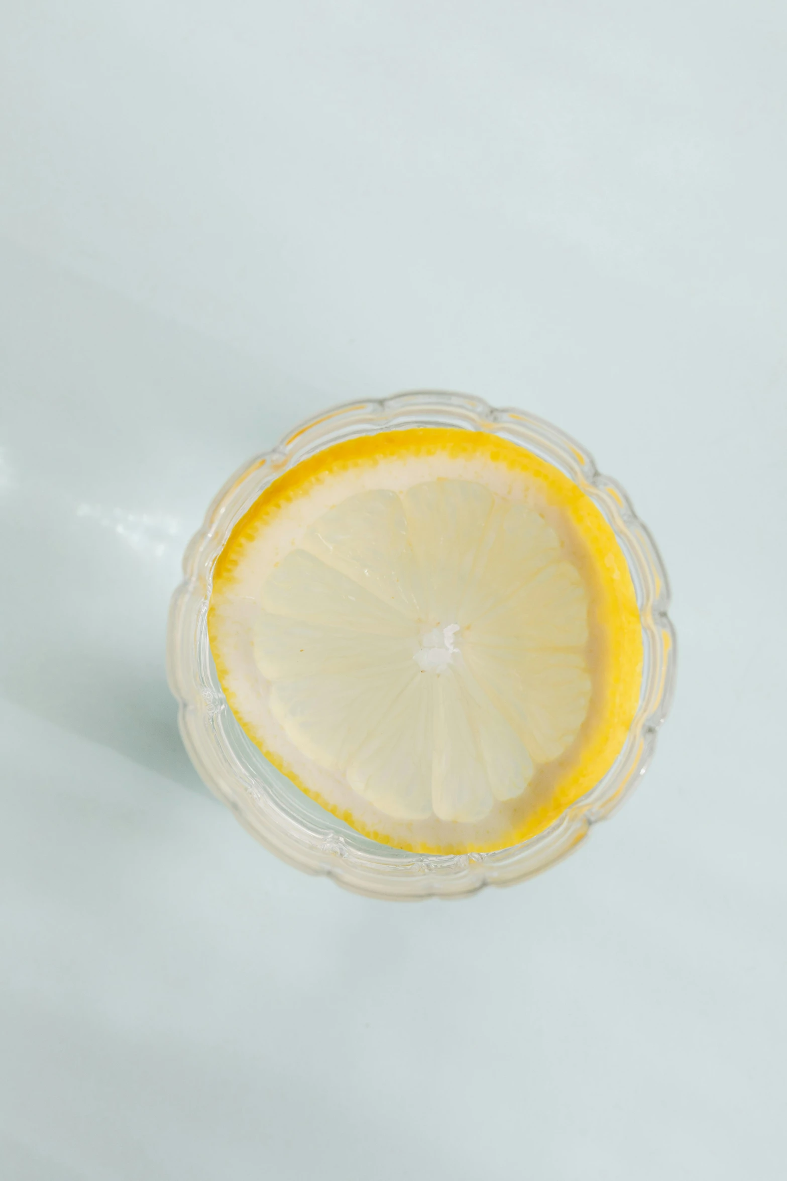 a glass of water with a slice of lemon in it, top - down view, detailed product image, lumi, opaque glass