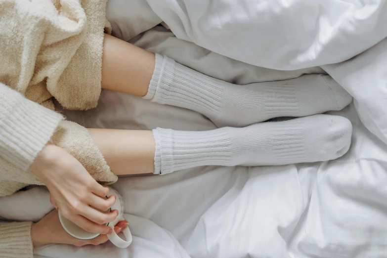 a woman laying in bed with a cup of coffee, inspired by Sarah Lucas, trending on pexels, wearing kneesocks, wearing white clothes, holding each other hands, gif