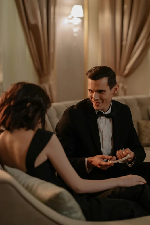 a man and a woman sitting on a couch, by Emma Andijewska, pexels contest winner, romanticism, gentlemens dinner, holds playing cards, elegant smiling pose, nathan for you