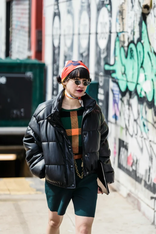 a woman walking down a sidewalk next to a graffiti covered wall, trending on pexels, model wears a puffer jacket, at new york fashion week, french bob, hong june hyung