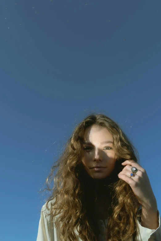 a woman with long curly hair talking on a cell phone, an album cover, unsplash, photorealism, clear blue sky, jewelry, soft light.4k, portrait sophie mudd