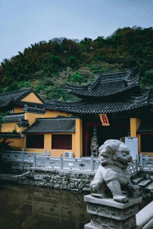 a stone lion statue in front of a yellow building, a statue, inspired by Yang Buzhi, beside the river, moody setting, roofs, 2000