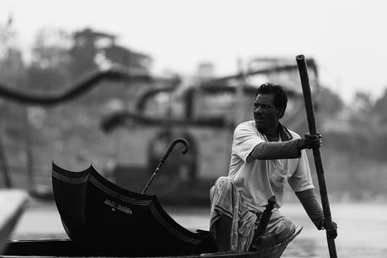 a man sitting in a boat with an umbrella, a black and white photo, by Sunil Das, pexels contest winner, holding a scythe, a handsome, information, holding a staff