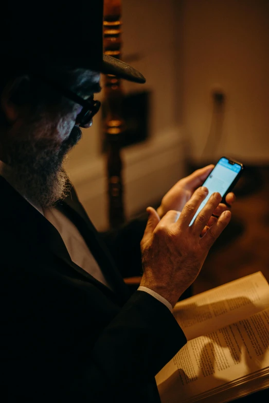 a man reading a book while holding a cell phone, a hologram, by Emanuel Witz, pexels, old gigachad with grey beard, tipping his fedora, eliezer yudkowsky, low-light