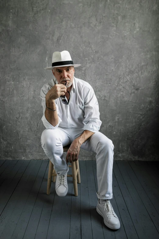 a man sitting on top of a wooden chair, a portrait, inspired by Agustín Fernández, pexels contest winner, white suit and hat, smoking with squat down pose, colin hay, white and silver
