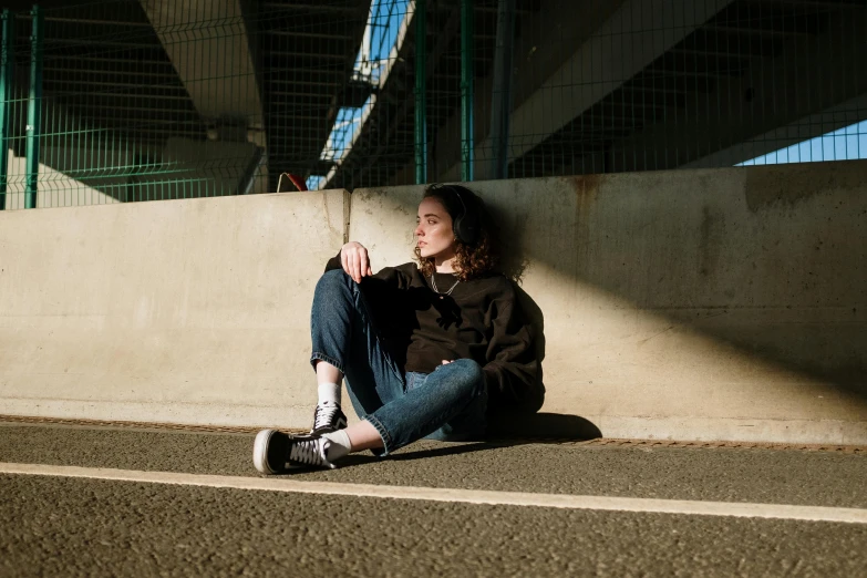 a woman sitting on the side of a road, pexels contest winner, wearing jeans and a black hoodie, miles johnstone, on the concrete ground, in a sunbeam