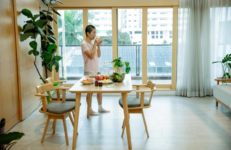 a woman standing in a living room next to a table, by Jang Seung-eop, pexels contest winner, dining table, healthy, balcony scene, asian male