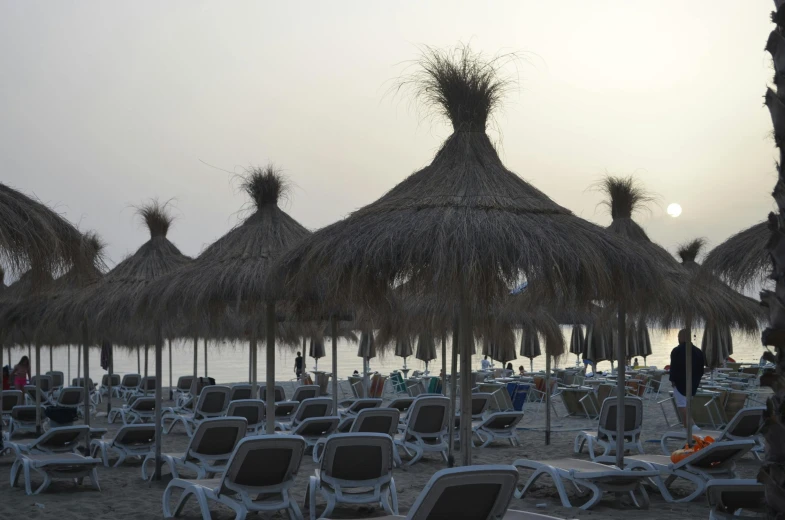 a number of chairs and umbrellas on a beach, a portrait, unsplash, marbella, unedited, in the evening, thatched roofs