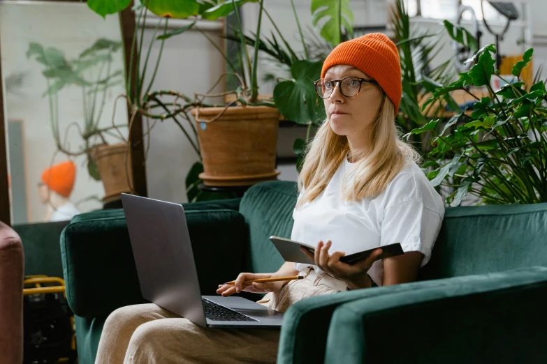 a woman sitting on a couch with a laptop, by Carey Morris, trending on pexels, renaissance, wearing a beanie, plants in glasses, avatar image, student