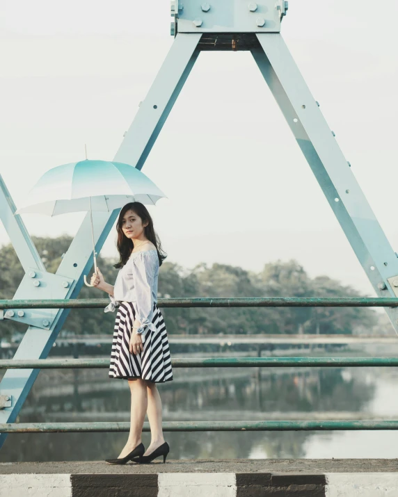 a woman standing on a bridge holding an umbrella, inspired by Cheng Jiasui, unsplash, striped pantyhose, teal skirt, wearing off - white style, looking confident