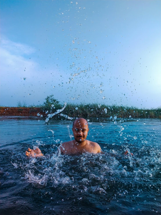 a man swimming in a body of water, covered in water drops, in a pond