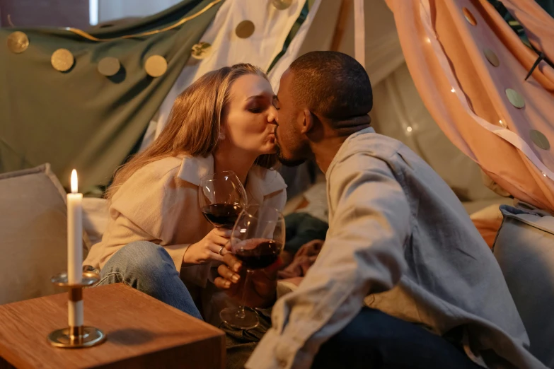 a man kissing a woman with a glass of wine, pexels contest winner, interior of a tent, bisexual lighting, brown, cute scene