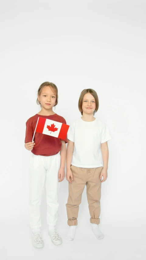 two children standing next to each other holding a canadian flag, pexels, white shirts, thumbnail, average, brown