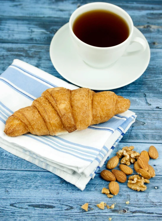 a croissant on a napkin next to a cup of coffee, shutterstock contest winner, 2 5 6 x 2 5 6 pixels, nut, blue, spanish