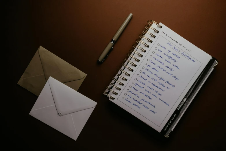 a notepad sitting on top of a desk next to a pen, by Julia Pishtar, unsplash, brown and white color scheme, magic list, email, late evening