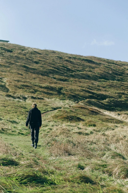 a man walking up a grassy hill on a sunny day, by Ceri Richards, unsplash, moorland, film photo, coastal, autumnal