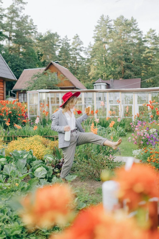 a woman in a red hat standing in a garden, inspired by Carl Larsson, pexels contest winner, in bloom greenhouse, full - length photo, finland, flowery cottage