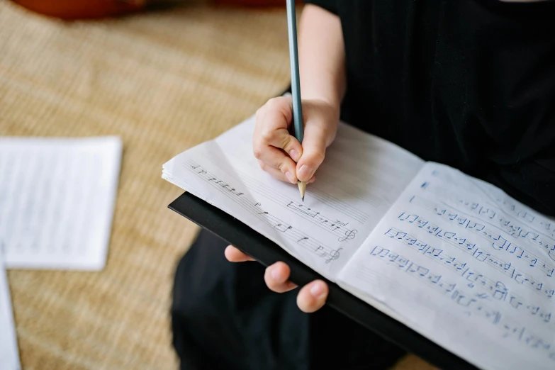 a person holding a pen and writing on a piece of paper, an album cover, by Julia Pishtar, unsplash, sheet music, sydney hanson, private school, holding a staff