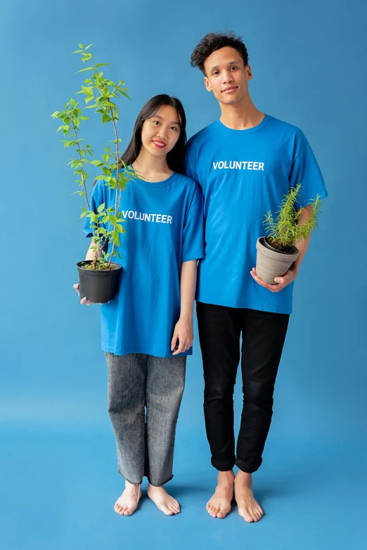 a man and woman standing next to each other holding plants, pexels contest winner, blue tight tshirt, 2 colour print, blue uniform, teenager