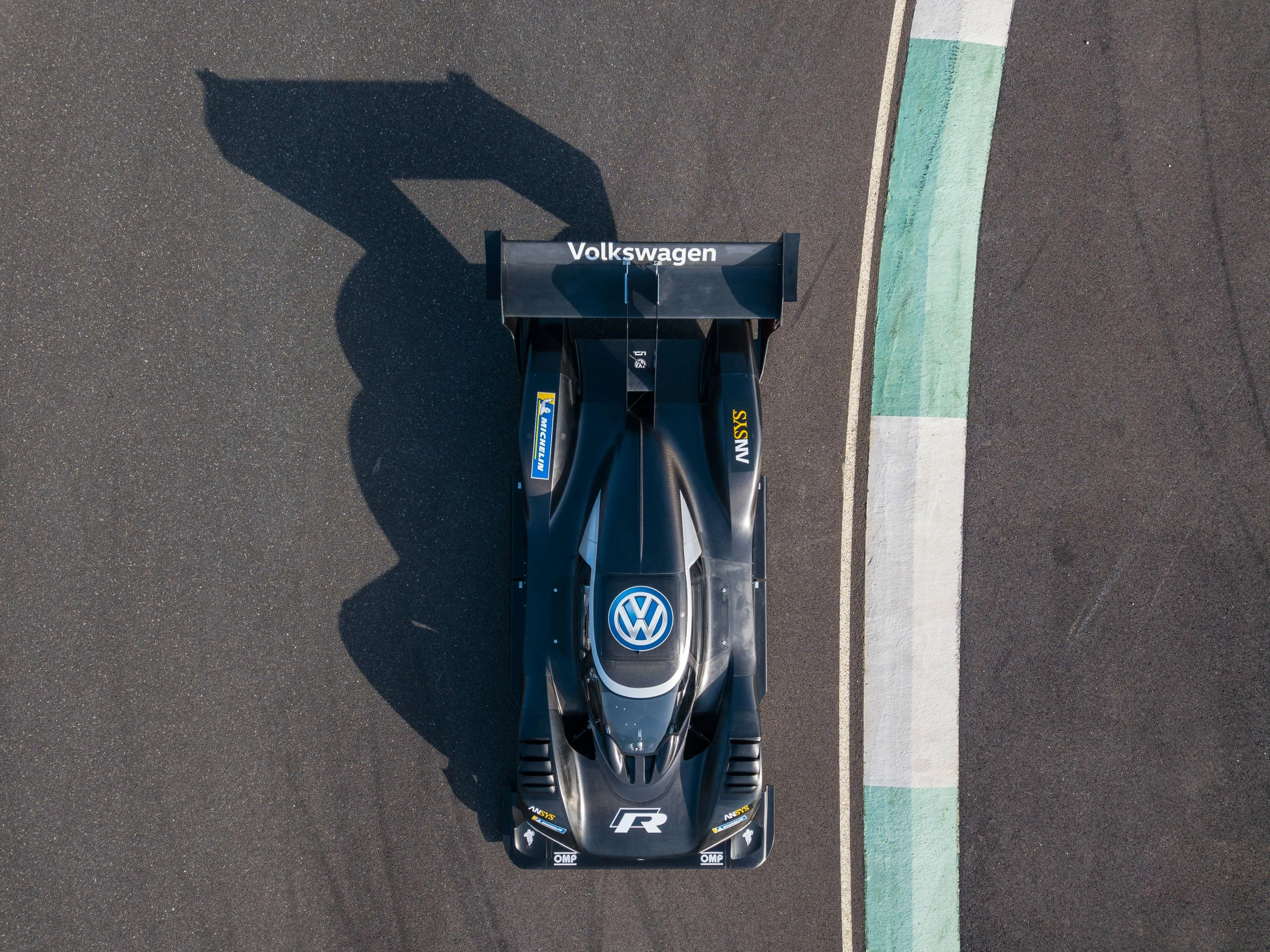 a close up of a race car on a track, wrapped in black, shot from drone, renaissance nimbus overhead, v wing