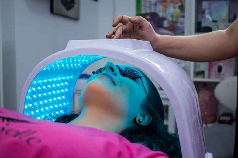 a woman getting a tanning treatment in a beauty salon, by Évariste Vital Luminais, pexels contest winner, massurrealism, blue leds, halo over her head, jelly glow, hospital lighting