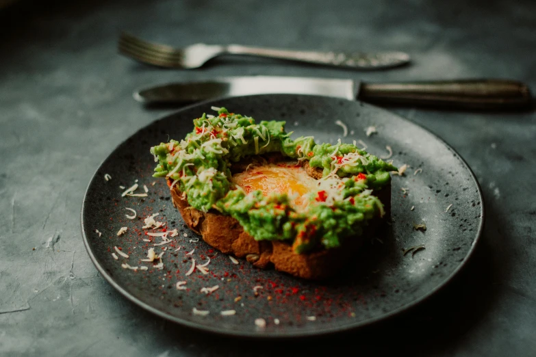 a black plate topped with a sandwich covered in guacamole, by Alice Mason, pexels contest winner, glowing moss, an egg, pointè pose, daily specials