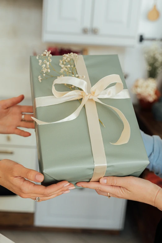 a woman giving a gift to another woman, by Eden Box, ribbons and flowers, hands pressed together in bow, square, holiday season