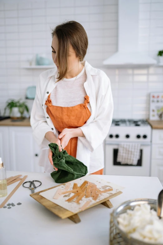 a woman in an orange apron preparing food in a kitchen, by Julia Pishtar, trending on pexels, fluid bag, copper and emerald, white, gif