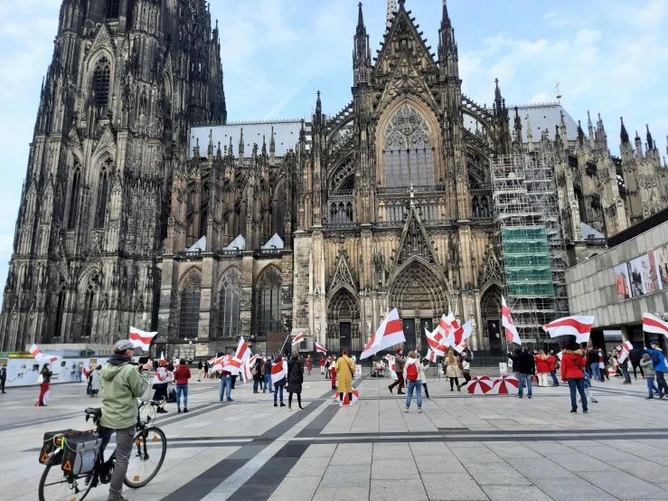 a man riding a bike in front of a cathedral, happening, red and black flags, protesters holding placards, german renaissance architecture, 🦩🪐🐞👩🏻🦳