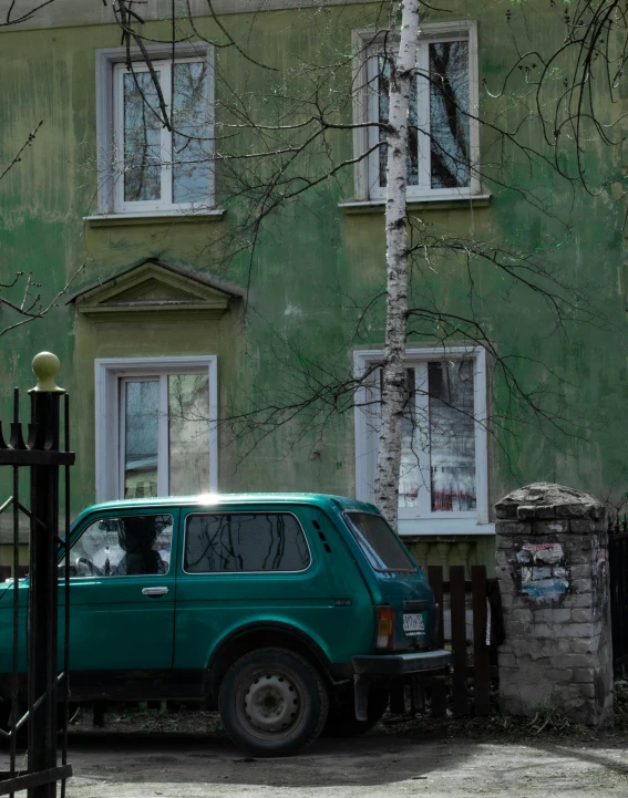 a green car parked in front of a green building, inspired by Isaac Levitan, pexels contest winner, socialist realism, before a stucco wall, фото девушка курит, during spring, in a square