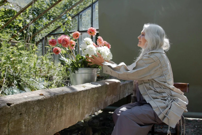 a woman sitting at a table with a bunch of flowers, natural light outside, an elderly, profile image, gardening