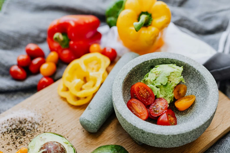 a wooden cutting board topped with a bowl of fruit and vegetables, by Julia Pishtar, pexels contest winner, mortar and pestle, avocado, multi - coloured, grey