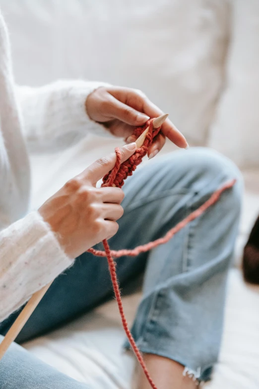 a woman is sitting on a couch knitting, trending on pexels, arts and crafts movement, red sweater and gray pants, spinning, holding a wooden staff, wearing a white sweater