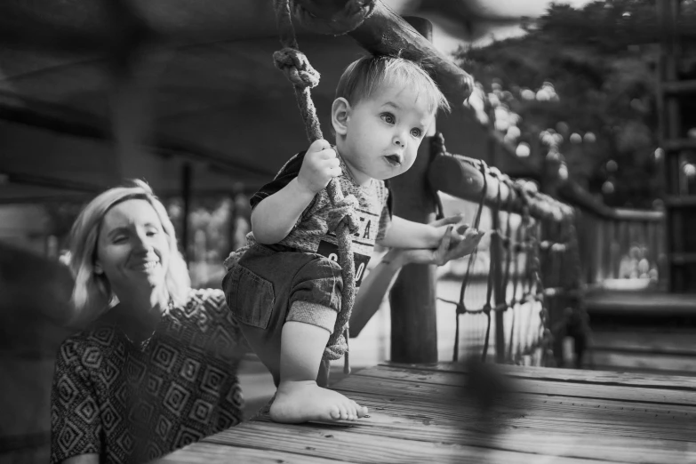 a black and white photo of a woman and a baby, by Joze Ciuha, pexels contest winner, on a birdge, cute boy, swings, innocent look