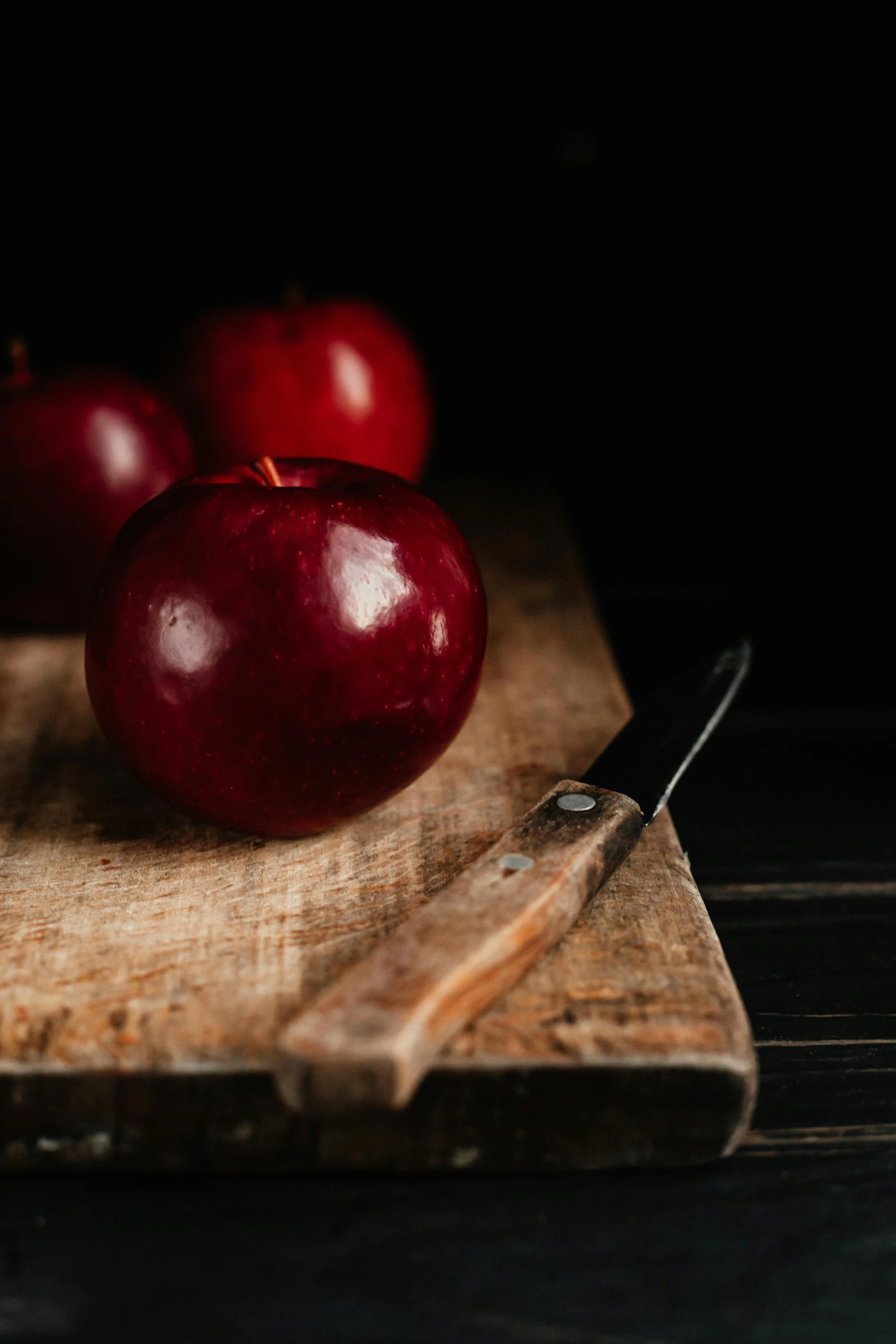 a wooden cutting board topped with three red apples, a still life, pexels, dark red, ((still life))