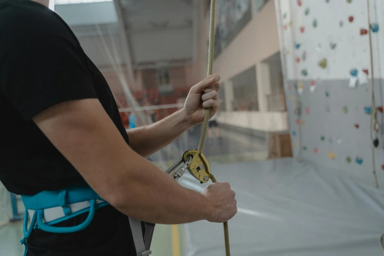 a man holding a rope in front of a climbing wall, indoor picture, photograph taken in 2 0 2 0, aerial silk, low quality photo