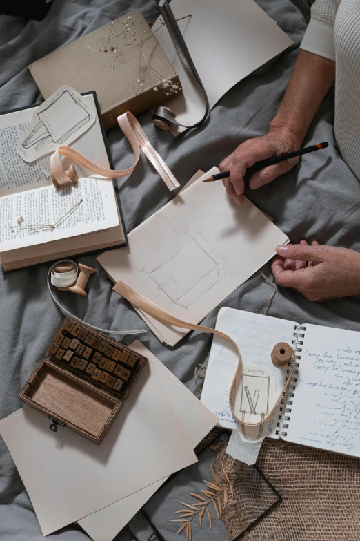 a woman sitting on top of a bed next to a pile of books, a still life, inspired by Leonardo da Vinci, trending on unsplash, process art, aerial view. hand stitching, writing on a clipboard, leather straps, neutral colours