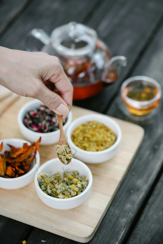 a wooden cutting board topped with bowls of food, pexels, process art, assam tea garden setting, partially cupping her hands, apothecary, white