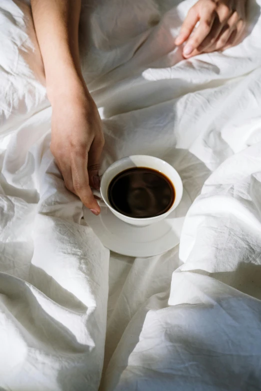 a person laying in bed with a cup of coffee, made of lab tissue, rum, linen, sleek hands