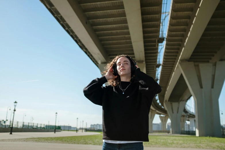a man standing under a bridge talking on a cell phone, an album cover, trending on pexels, realism, timothee chalamet, black hoodie techie, girl wearing headphones, doing a majestic pose