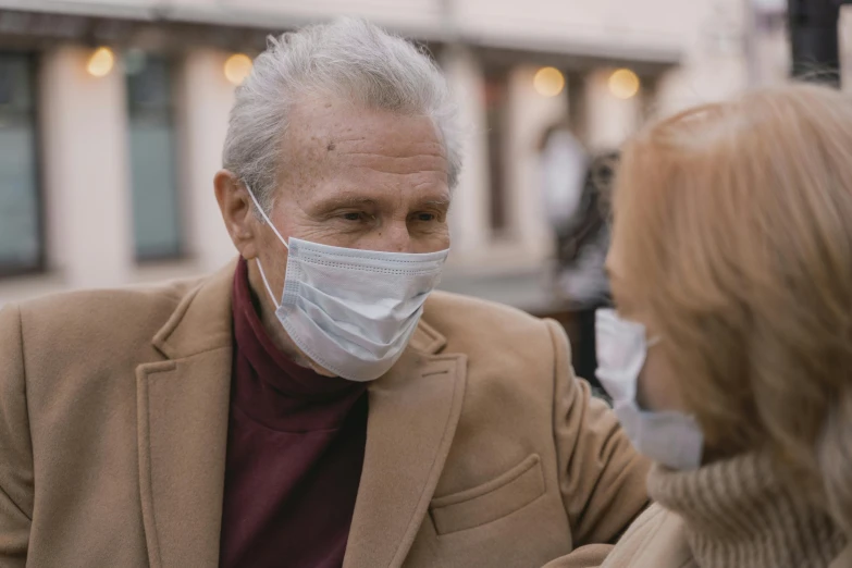 a man in a face mask talking to a woman, a photo, pexels, gray haired, fan favorite, brown, 3 - piece