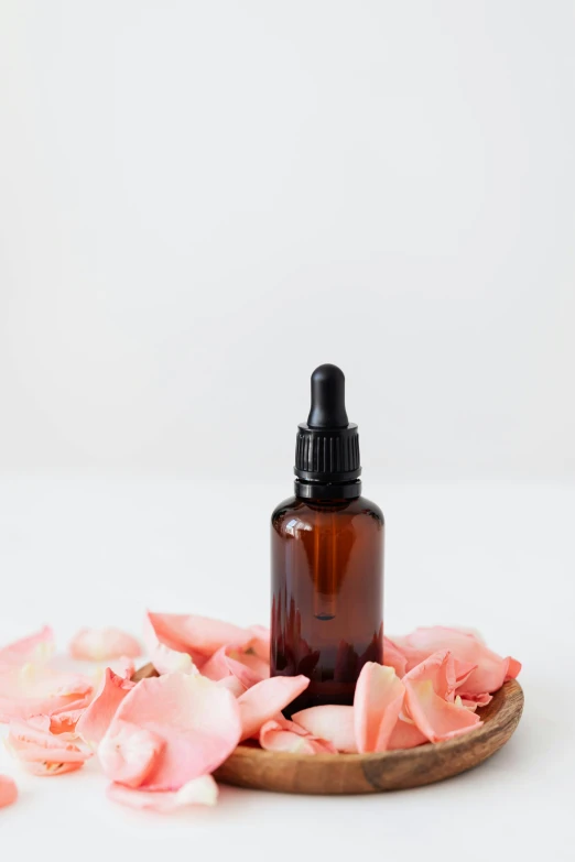 a bottle of essential oil next to rose petals, unsplash, set against a white background, thumbnail, amber, 1 6 x 1 6