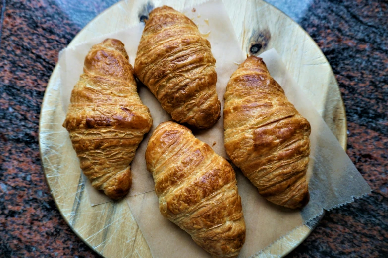 three croissants on a plate on a table, a portrait, by Tom Wänerstrand, pexels, hurufiyya, on a wooden tray, taken on iphone 14 pro, thumbnail, wrinkly