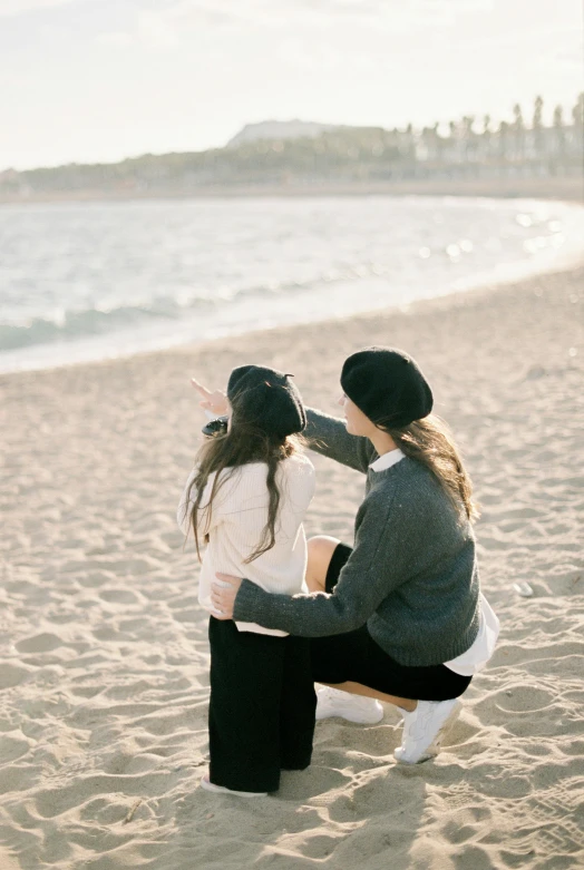 a couple of people sitting on top of a sandy beach, a picture, by Lucia Peka, trending on unsplash, daughter, ulzzang, lesbian, warmly lit