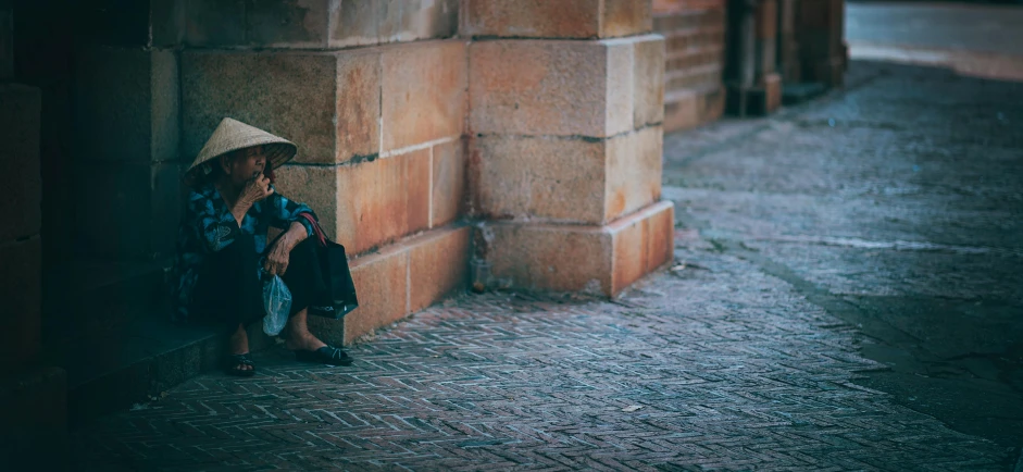 a woman sitting against a brick wall talking on a cell phone, by Adam Marczyński, pexels contest winner, realism, bags on ground, vietnamese woman, a pilgrim, in a square