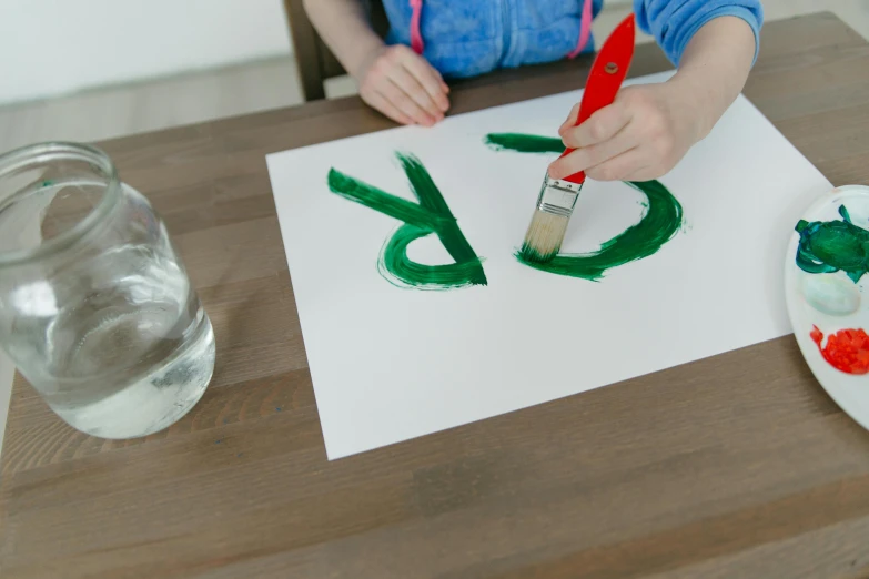 a child is painting on a piece of paper, inspired by Howard Hodgkin, pexels, green letters, made of drink, on a white table, teaser